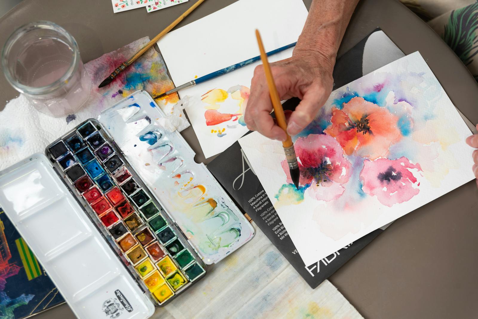 An artist skillfully painting vibrant flowers using watercolor on paper, showcasing creative artistry.