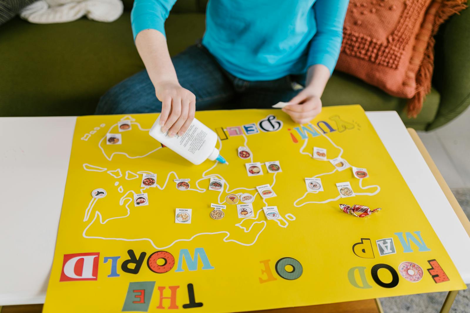 Person creating a colorful world map art project on a poster board, crafting with cutout elements and glue.